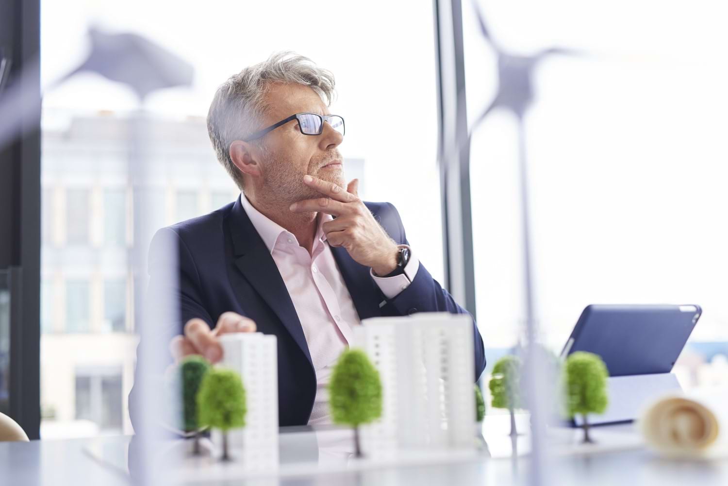 Ein Mann am Schreibtisch vor dem Modell einer grünen Siedlung: Nachhaltiges Bauen ist die wohl wichtigste Entwicklung in der Schweizer Baubranche.
