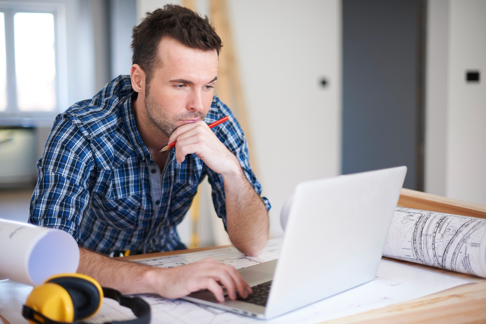 Ein Mann sitzt auf der Baustelle vor einem Laptop und bearbeitet Daten, mit denen er später den Jahresabschluss erstellen kann.
